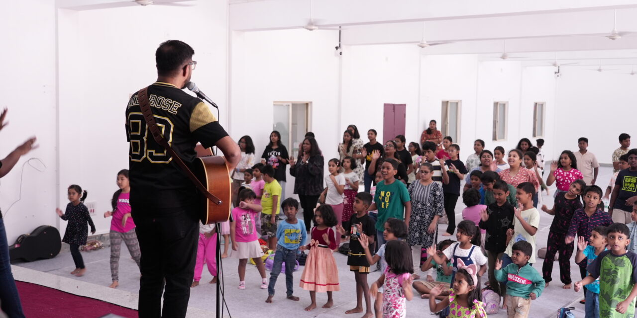 Musician playing a guitar and leading little children in praise and worship during a VBS program at City Harvest Church