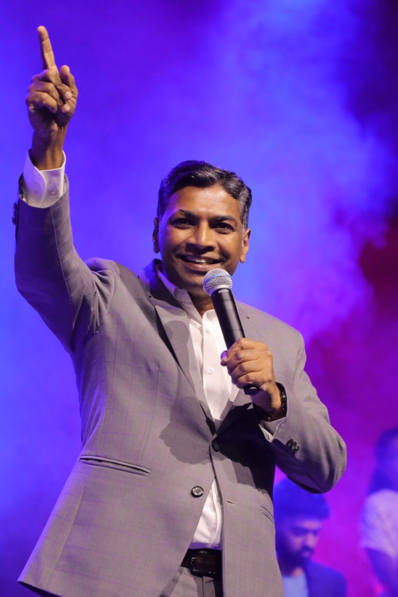 A pastor preaching to the congregation with a blue background.