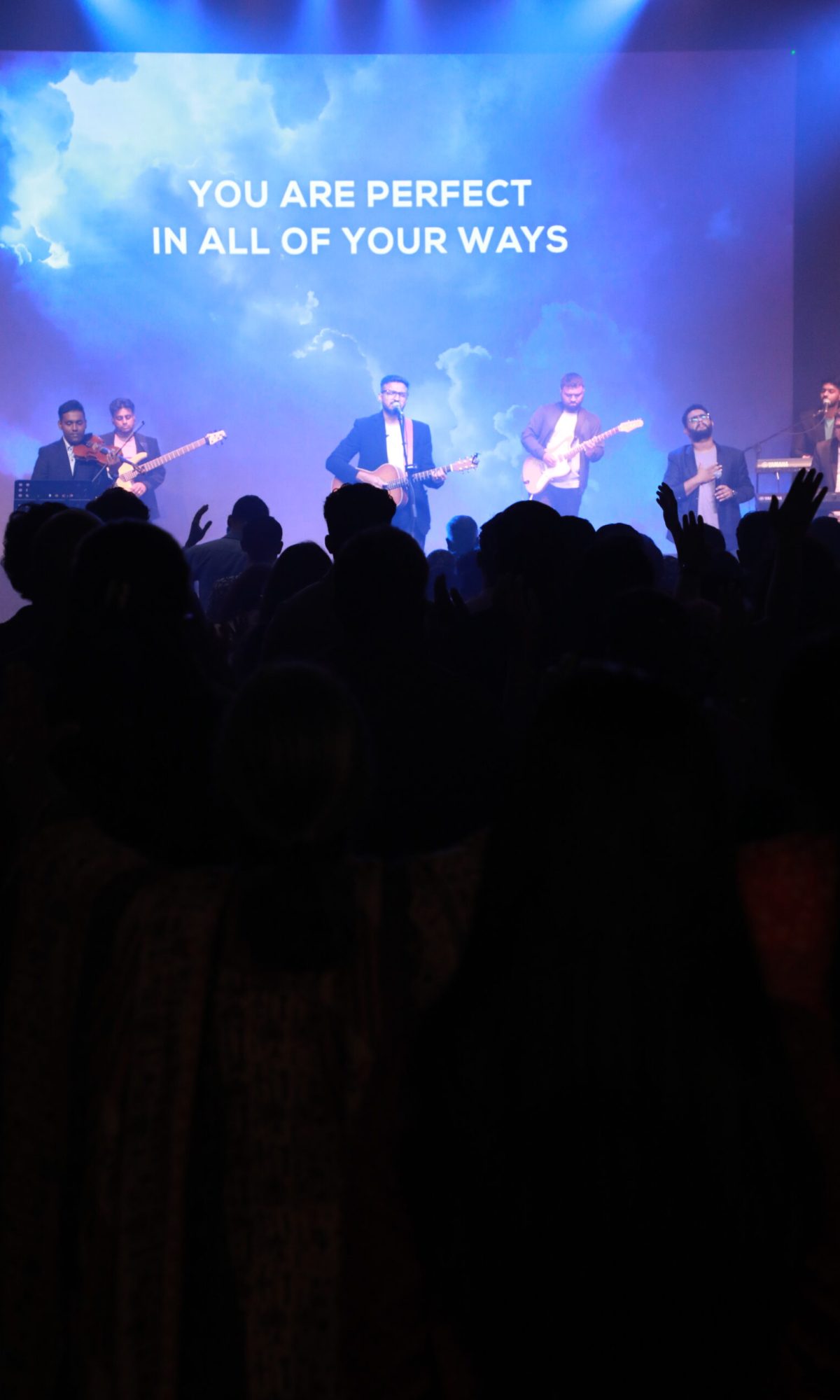 Worship leader and musicians leading the praise and worship session in front of a blue background.